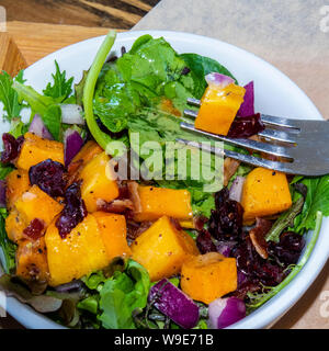 Une fraîche et les fruits et noix salade dans un bol avec une fourchette tenant un morceau de mangue. Banque D'Images