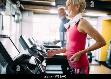 Happy senior des gens courir ensemble sur des tapis roulants dans une salle de sport. Banque D'Images
