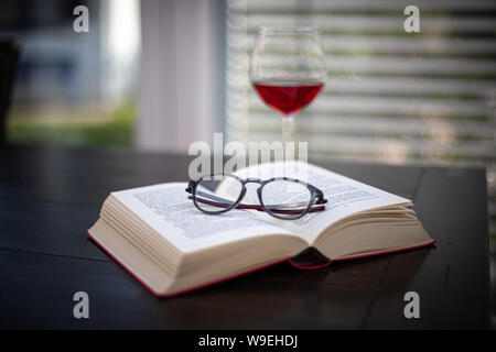 Une paire de lunettes se trouve sur un livre ouvert et à l'arrière-plan est un verre à vin Banque D'Images