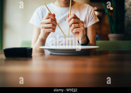 Paire de baguettes dans woman's hands, close-up. Jeune femme est assis à table dans le restaurant prépare à manger la nourriture japonaise. Banque D'Images