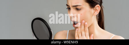 Choqué de femme avec l'acné sur le visage regardant mirror isolé sur gray Banque D'Images