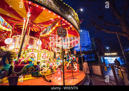 Des lumières rouges et jaunes brillantes sur un carrousel du parc des expositions brillent Dans une nuit bleue inky sur Londres Southbank près d'un kiosque à poisson et à copeaux le soir d'hiver Banque D'Images