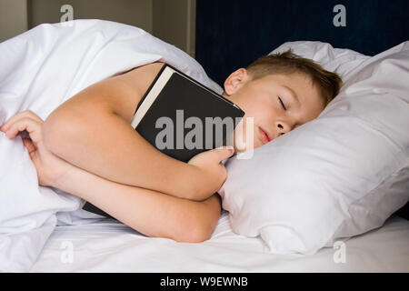 Adolescent fatigué sleeping in bed with book Banque D'Images