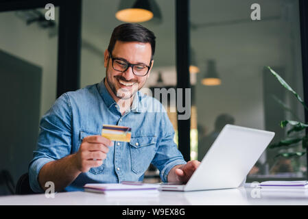 Happy happy smiling young adult man doing shopping en ligne ou e-shopping entrepreneur satisfait faire payer pour le service de paiement en ligne ou de marchandises se Banque D'Images