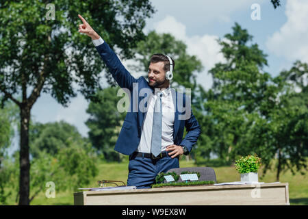 Jeune homme d'écouter de la musique dans les écouteurs et la danse de Park près de table avec piles Sun Mise en page et cache-pot Banque D'Images
