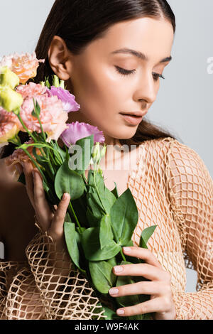 Belle jeune femme en maille beige holding bouquet de fleurs eustoma et regardant en bas isolé sur gray Banque D'Images