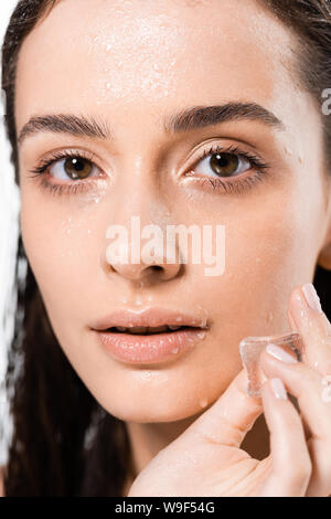 Portrait de jeune femme tenant humide brunette ice cube et looking at camera isolated on white Banque D'Images