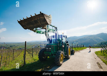 Alsace, France - Apr 19, 2019 - Vue avant du tracteur John Deere excavatrice 6100 stationné dans un vignoble avec woman silhouette en arrière-plan Banque D'Images