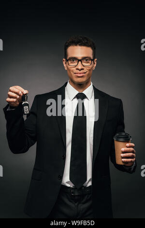 Happy african american businessman holding car keys et du café pour aller sur fond sombre Banque D'Images