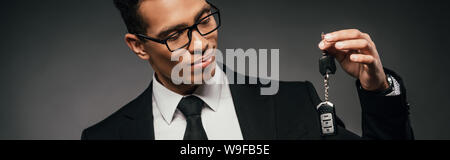 Smiling african american businessman looking at clés de voiture sur fond sombre, vue panoramique tourné Banque D'Images