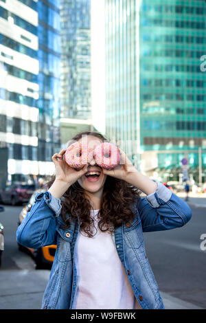 Smiling Funny Girl et donut rose lunettes dans une grande ville Banque D'Images