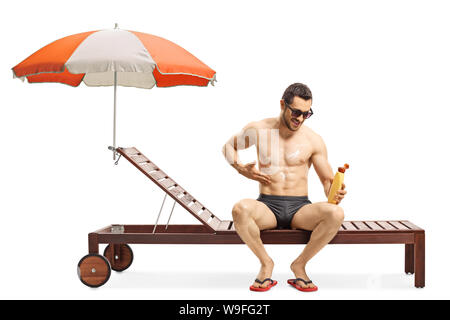 Longueur totale d'un bel homme en appliquant une crème solaire et assis sur une chaise longue sous égide isolé sur fond blanc Banque D'Images