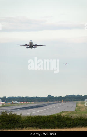 Un avion décolle comme d'autres entrent en terre dans une file d'atterrissage d'avion derrière, avec d'autres avions en attente à côté de la piste de décollage. Banque D'Images