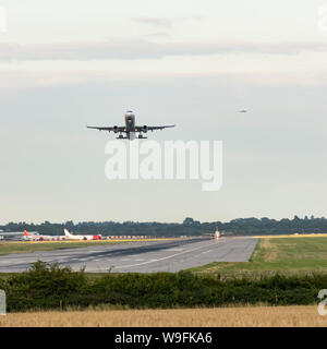 Un avion décolle comme d'autres entrent en terre dans une file d'atterrissage d'avion derrière, avec d'autres avions en attente à côté de la piste de décollage. Banque D'Images