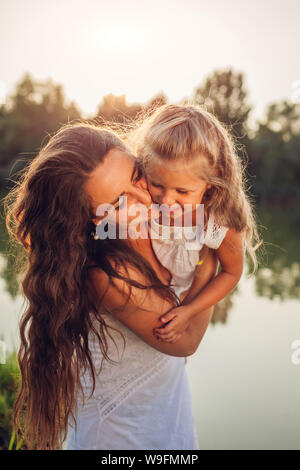Le jeu et le plaisir de la mère avec la fille par la rivière d'été au coucher du soleil. Woman holding kid, chatouillant et rire. Les valeurs de la famille Banque D'Images
