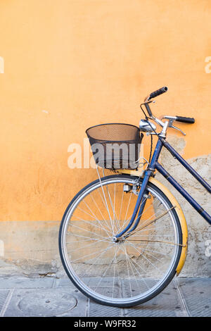 Un vélo bleu marine avec un panier appuyé contre un mur orange à Pise, Italie. Banque D'Images