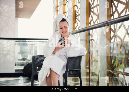 Concept de relaxation et de communication après spa. Portrait de jeune femme en peignoir de parler par téléphone sur terrasse Banque D'Images