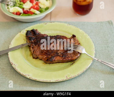 Ribeye Steak, grillé, servi sur une plaque verte et napperon. Les ustensiles et une salade mixte. Banque D'Images