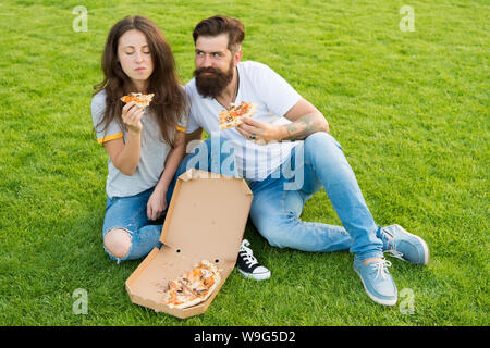 Les amateurs de pizza. heureux couple eating pizza. couple in love dating. restauration rapide. barbu hipster et adorable fille manger une pizza. week-end en famille. été pique-nique sur l'herbe verte. Banque D'Images