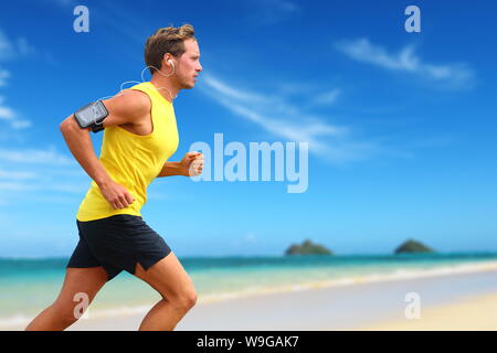 L'écoute du canal de musique smartphone fonctionnant sur la plage. Lanikai, Oahu, Hawaii, USA. La course à l'athlète masculin de l'océan ou sur la plage au bord de l'élaboration avec smart phone app device et écouteurs en été. Banque D'Images