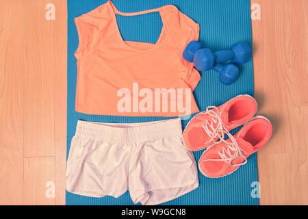 Vêtements d'entraînement - fitness tenue et chaussures de course. Passage de vêtements prêt à soulever des poids dans la salle de sport ou à la maison, allongé sur un tapis de yoga sur le sol. Matching orange t-shirt et espadrilles. Banque D'Images