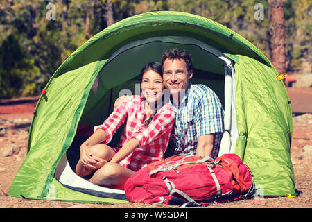 Happy young couple sitting in tent. Les randonneurs, hommes et femmes sont au repos dans la tente. Les jeunes sont partenaires avec le sac de randonnée journée ensoleillée. Banque D'Images