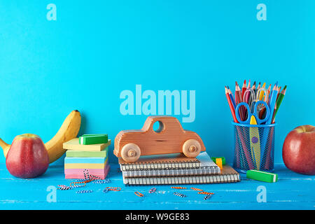 Ensemble de fournitures scolaires : bloc-notes, crayons, autocollants, trombones, ciseaux et d'un jouet en bois voiture rétro sur fond bleu, concept de nouveau à l'école Banque D'Images