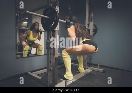 La formation de l'athlète féminine dans une salle de sport avant de miroir. Carrossier dans le sport top et short d'entraînement fonctionnel faisant poids de levage. Jolie femme Banque D'Images