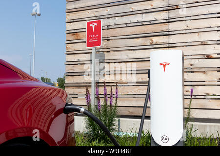 Tesla Model S rouge branché en milieu urbain, la recharge chez Tesla Supercharger. Banque D'Images