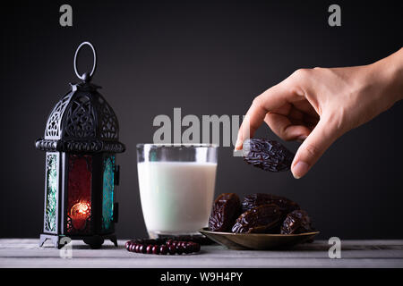 Ramadan nourriture et boissons concept. La femme s'adresse à une plaque avec date avec le Ramadan avec Lanterne Lampe arabe, Chapelet en bois, thé, fruits et dates Banque D'Images