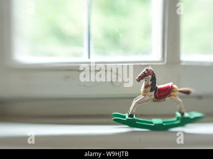 Cheval à bascule miniature en bois anciens se balançant dans l'appui de fenêtre d'une vieille fenêtre en bois blanc Banque D'Images
