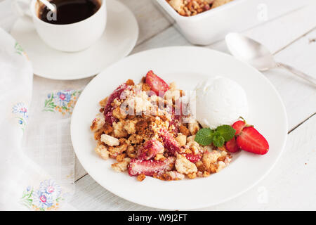Crumble aux fraises servi avec de la crème glacée, des fraises fraîches et de feuilles de menthe sur la table rustique blanc Banque D'Images