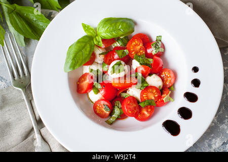 Vue de dessus de salade fraîche avec de la mozzarella, tomates cerises et de feuilles de basilic on white plate Banque D'Images