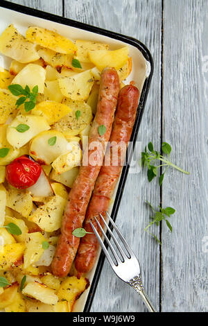 Pomme de terre cuite au four avec des tranches de tasy poêlée de saucisses de Munich avec des feuilles de basilic sur une plaque de cuisson Banque D'Images