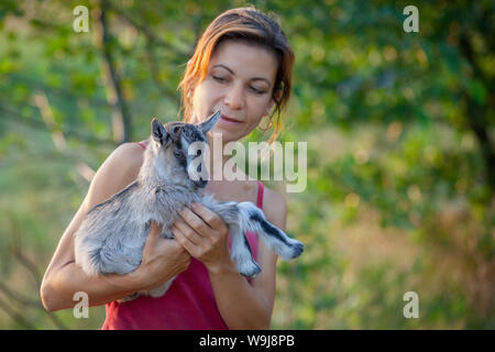 Belle femme avec un joli petit goatling sur ses mains dans un fond vert Banque D'Images