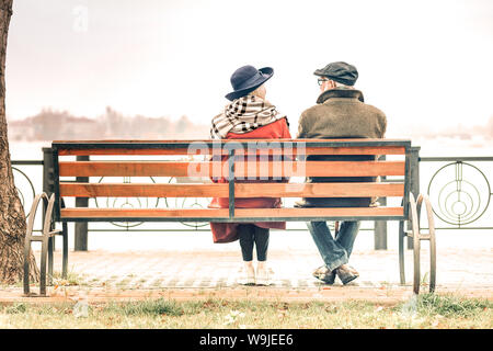 Vue arrière d'un senior couple sitting on bench in autumnal park Banque D'Images