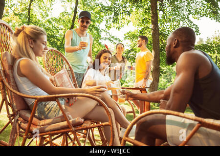 Groupe des amis de la bière et heureux d'avoir un barbecue de travail à jour ensoleillé. Ensemble de repos dans une forêt en plein air ou glade jardin. Célébrer et relaxant, laughting. Vie d'été, l'amitié concept. Banque D'Images