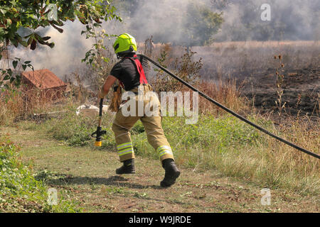 Les Pompiers au travail s'attaque à un feu sur le terrain et en tirant un arrosage Banque D'Images