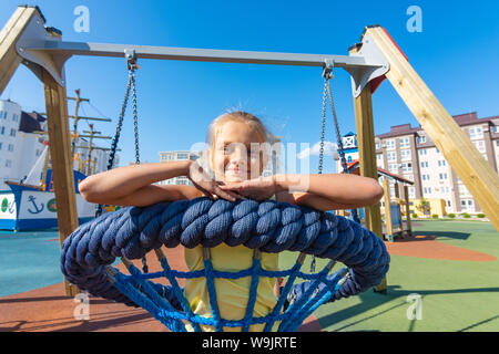 Girl riding a round pendaison swing dans l'aire de jeux Banque D'Images