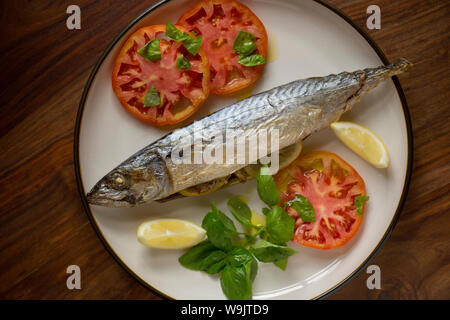 Un maquereau (Scomber scombrus), qui a été cuit en papillote et servi avec des tranches de tomate, basilic, huile d'olive et des quartiers de citron. C'est farci de Banque D'Images