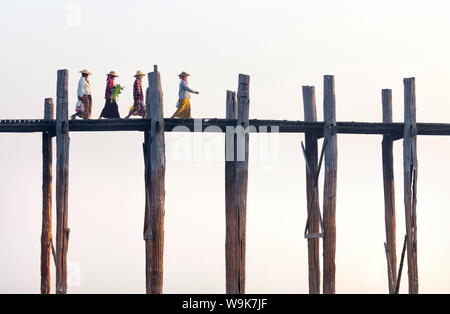 Les femmes locales de marcher à travers U Bein Bridge derrière, la plus longue du monde pied teck pont sur le lac Taungthaman, Amarapura, près de Mandalay, Myanmar Banque D'Images