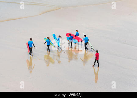 Les surfeurs débutants avec leurs planches de marcher pour commencer une leçon de surf à grande Gt. Plage de l'ouest à Newquay en Cornouailles. Banque D'Images