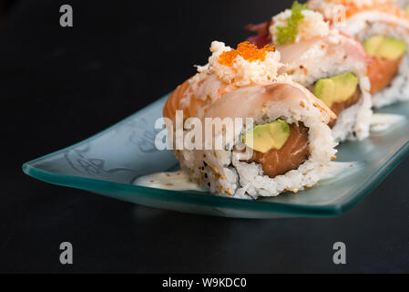 Uramaki spécial, le riz farci au saumon avocat, couverts de sashimi de thon rouge et la mer basse, assaisonné de sauce au fromage, black backgroun Banque D'Images