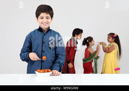 Boy eating gulab jamun with his friends playing in the background Stock Photo