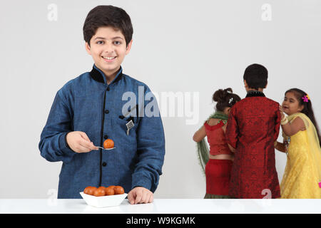 Boy eating gulab jamun with his friends playing in the background Stock Photo