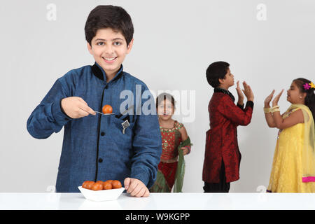 Boy eating gulab jamun with his friends playing in the background Stock Photo