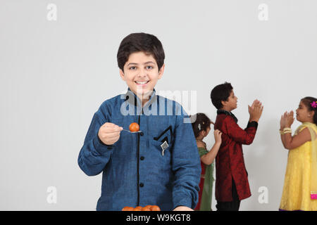 Boy eating gulab jamun with his friends playing in the background Stock Photo