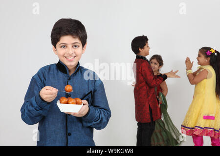 Boy eating gulab jamun with his friends playing in the background Stock Photo