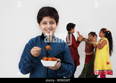 Boy eating gulab jamun with his friends playing in the background Stock Photo