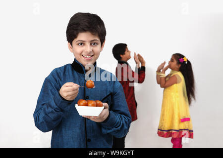 Boy eating gulab jamun with his friends playing in the background Stock Photo